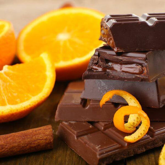 Stacked dark chocolate bars with orange slices and orange peel curls on wooden surface representing Chocolate Orange Scented Soy Wax Candle fragrance
