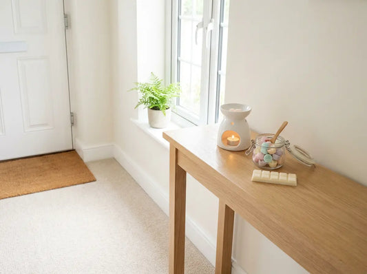 Wax melt snap bar, open tub of wax melt scoopies and a white tealight burner on a hallway console table in a bright, airy home.