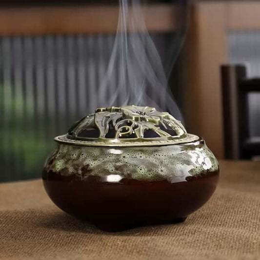 Green ceramic incense burner kiln with decorative lid releasing smoke on a table